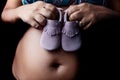 Detail of pregnant woman holding baby shoes against her belly