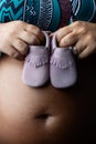 Detail of pregnant woman holding baby shoes against her belly