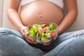 Detail of a pregnant woman sitting with a fresh salad bowl in her lap