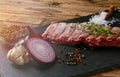 Detail raw wild boar meat on a black plate with garlic, rosemary, onion salt and pepper