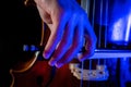 Detail of the right hand holding a cello bow while playing classical music with artistic illumination of blue led light