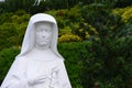 Detail of sculpture of polish Saint Faustyna Kowalska holding cross and rosary, decorative shrubs in background. Royalty Free Stock Photo