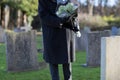 Close Up Of Senior Woman With Flowers Standing By Grave