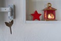 Detail of a shelf with christmas decoration in a white wall, red star and lamp with candle light Royalty Free Stock Photo