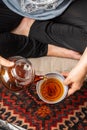 Detail shot of mature woman in comfortable clothes serving tea in a cup, on gray cushion on carpet