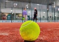 Detail shot of a paddle ball on the floor of the indoor paddle tennis court and three player friends in the background