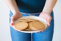 A detail shot of woman's hands with red nails holding a plate of simple delicious cookies, white background