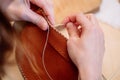 Detail shot of woman`s hands sewing a brown piece of leather with a needle