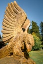 Detail shot of wooden sculpture of bird of prey with trees and blue sky in the background.