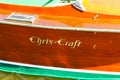 Detail of side of a classic wood Chris-Craft boat with logo painted on wood and water lapping bottom visible at bottom