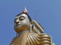 A detail of a sitting Buddha opposite a blue sky