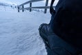 Detail of a snow boot with crampons walking on a totally snowy path in Iceland with the railing of a road fence frozen by the