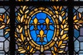 Detail of stained glass panel with gold leaves, three gold fleur de lys on blue background, symbol used in heraldry