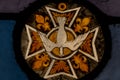 Detail of stained glass panel with gold Maltese cross, white dove, four gold fleur de lys