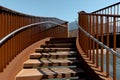 Detail of a stairway of a modern rusty bridge, with a clear blue sky behind it. Strong contrast between lights and shadows