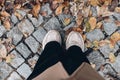 Detail of standing woman. Female legs in black trousers and pink sneakers. Cobblestone pavement, road with dry maple Royalty Free Stock Photo