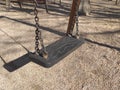 Detail of swing bench with metal ropes on sand ground of playground. Closeup of plastic gray swing for kids on the park