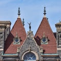 Detail of two equal red brick towers, in a stone building. In the middle, a decorative deer statue. Architecture concept A