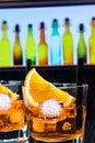 Detail of two glasses of spritz aperitif aperol cocktail with orange slices and ice cubes on bar table, disco atmosphere backgroun