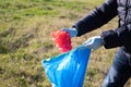 Detail of a volunteer's hand picking up a red plastic bag from the forest and putting it in a garbage bag. Concept of Earth Day