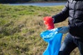 Detail of a volunteer's hand picking up a red plastic bag from the forest and putting it in a garbage bag. Concept of Earth