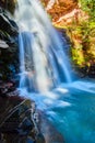 Detail of waterfall over cliffs with red rocks and moss into blue bucket of water Royalty Free Stock Photo