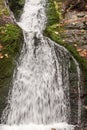 Detail of waterfall with rocks covered by moss and fallen leaves