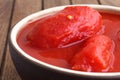 Detail of whole canned tomatoes in brown bowl.