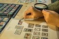 Detail of a woman is hands a magnifying glass and tweezers checking a stamp from her philatelic collection