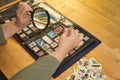 Detail of a woman is hands a magnifying glass and tweezers checking a stamp from her philately collection