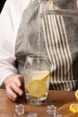 Detail of woman`s hand serving tonic in a glass with lemon slices, on wooden table with ice,