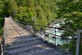 Detail of a wooden foot bridge over a mountain river with blue-green cold water, big stones and freen forest around Royalty Free Stock Photo