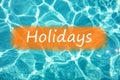 Detail of word `Holidays` on swimming pool water and sun reflecting on the surface