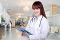 Detail of a young Asian woman doctor holding a clipboard standing on hospital background. health care concept