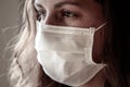 Detail of young Caucasian woman wearing a white medical face mask. Focus on the front part of the face, blurred background.