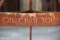 Detailed close up filled frame shot of an old weathered rusty warning sign saying in Cyrillic Russian DANGER ZONE