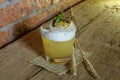 Detailed closed drink shot of a delicious fresh yellow punch cocktail with ice in a transparent glass standing on a wooden table