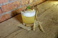 Detailed closed drink shot of a delicious fresh yellow punch cocktail with ice in a transparent glass standing on a wooden table