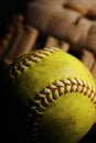 Closeup of a used, yellow softball resting in front of a brown glove. Royalty Free Stock Photo