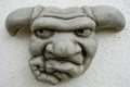 Detailed image of a stonework Gargoyle grimacing face, seen hanging on an outside wall.