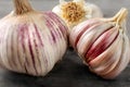 Detailed photo of garlic bulbs on wooden table, some purple cloves uncovered under garlic skin.