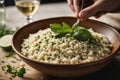 A detailed shot of a bowl of creamy risotto being garnished with fresh herbs