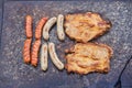 Detailed top view on the granite stone grill with two kind of sausages and pork collar steaks. Royalty Free Stock Photo