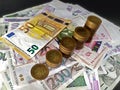 A detailed view of different types of euro banknotes arranged differently on a dark background, the banknotes have euro coins stac
