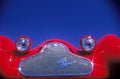 A detailed view of a highly polished chrome grill and bug eyed headlights on a red vintage Alpha Romeo sports car.