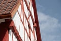 Detailed view of the upper part of a half-timbered house. You can see the roof peak against a blue sky. There are tiles on the