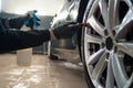 Detailing center worker cleans car wheels with brush. Vehicle wheel rim cleaning process.