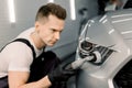 Detailing and polishing of car headlight on car. Young professional concentrated Caucasian male worker with orbital Royalty Free Stock Photo