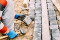 Details of construction works with industrial worker placing granite cobblestone blocks on path or alley