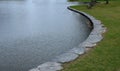 Details of the edge of the pond with paved banks flat stones. curved shape. the path is lined with weeping willows and the sluice Royalty Free Stock Photo